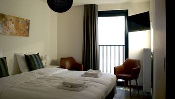 Een hotelkamer met een groot bed, twee stoelen, een flatscreen televisie en een schilderij aan de muur.