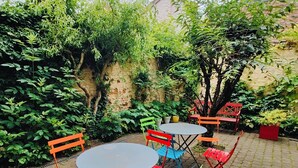 Patio esterno con pavimento in mattoni, circondato da vegetazione lussureggiante e un muro di mattoni.