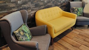 Un'area d'attesa moderna con una parete in legno a motivi a spina di pesce, due poltrone grigie e un divano giallo.
