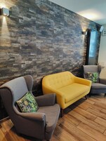 Un área de espera moderna con una pared de madera en patrón de espiga, dos sillones grises y un sofá amarillo.