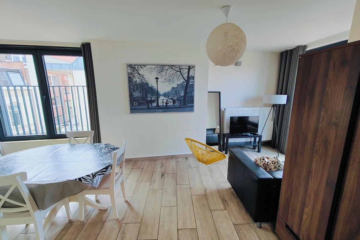 A modern living room with a dining area, a large window, a painting, a TV, and a wooden cabinet.