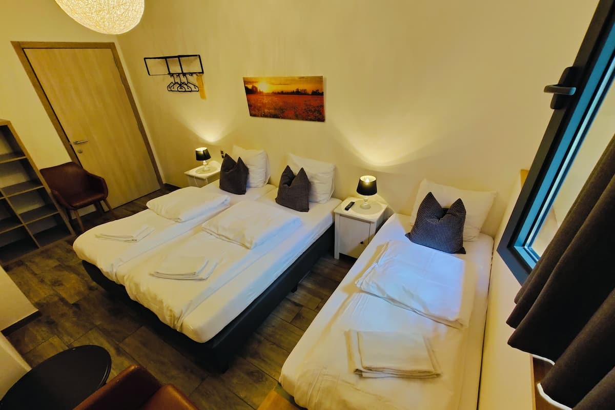 A hotel room with two beds, a chair, a small table, a nightstand with a lamp, and a painting on the wall.