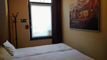 Una habitación de hotel con una cama, una ventana con cortinas, un perchero y un cuadro en la pared.