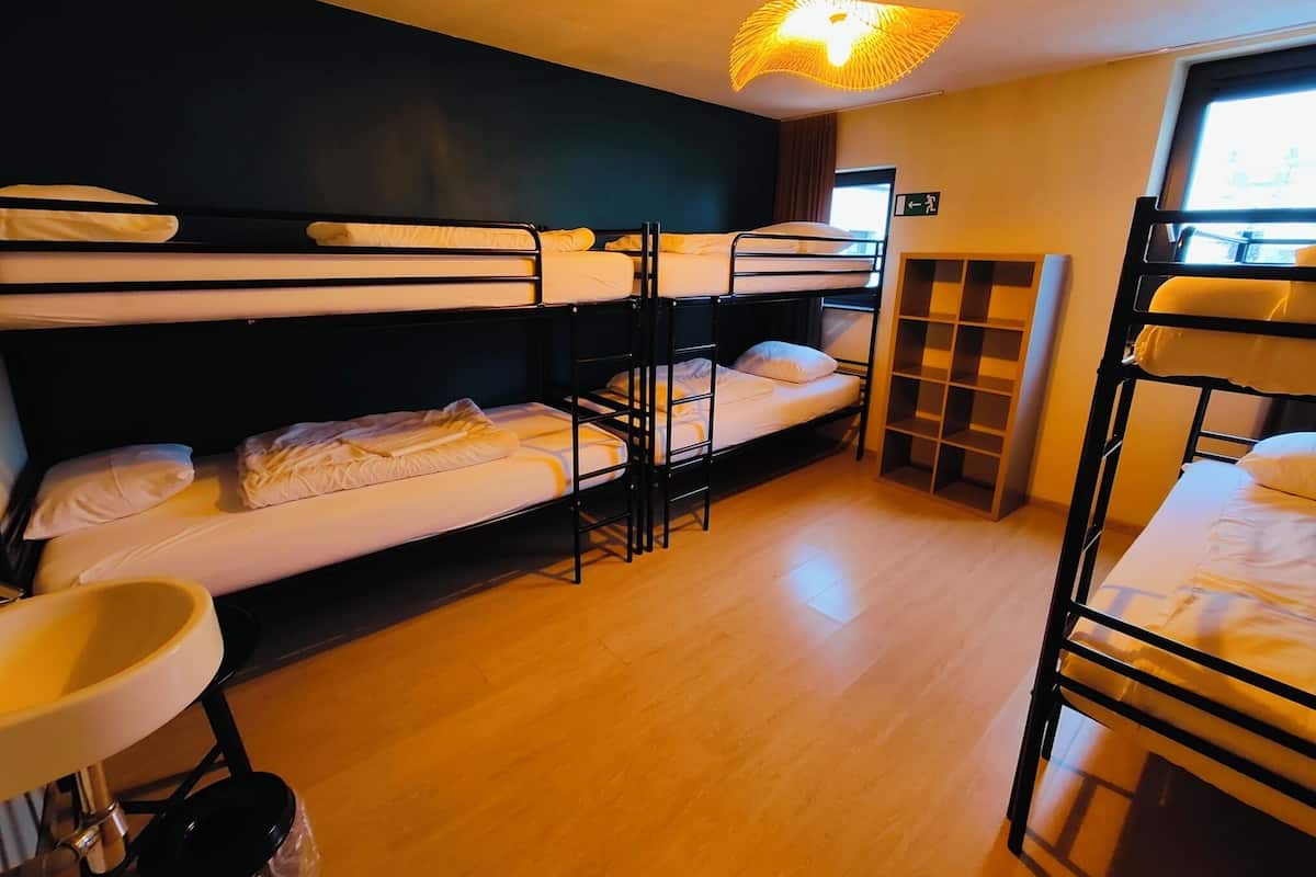 Un dormitorio con literas, un lavamanos pequeño y una estantería.
