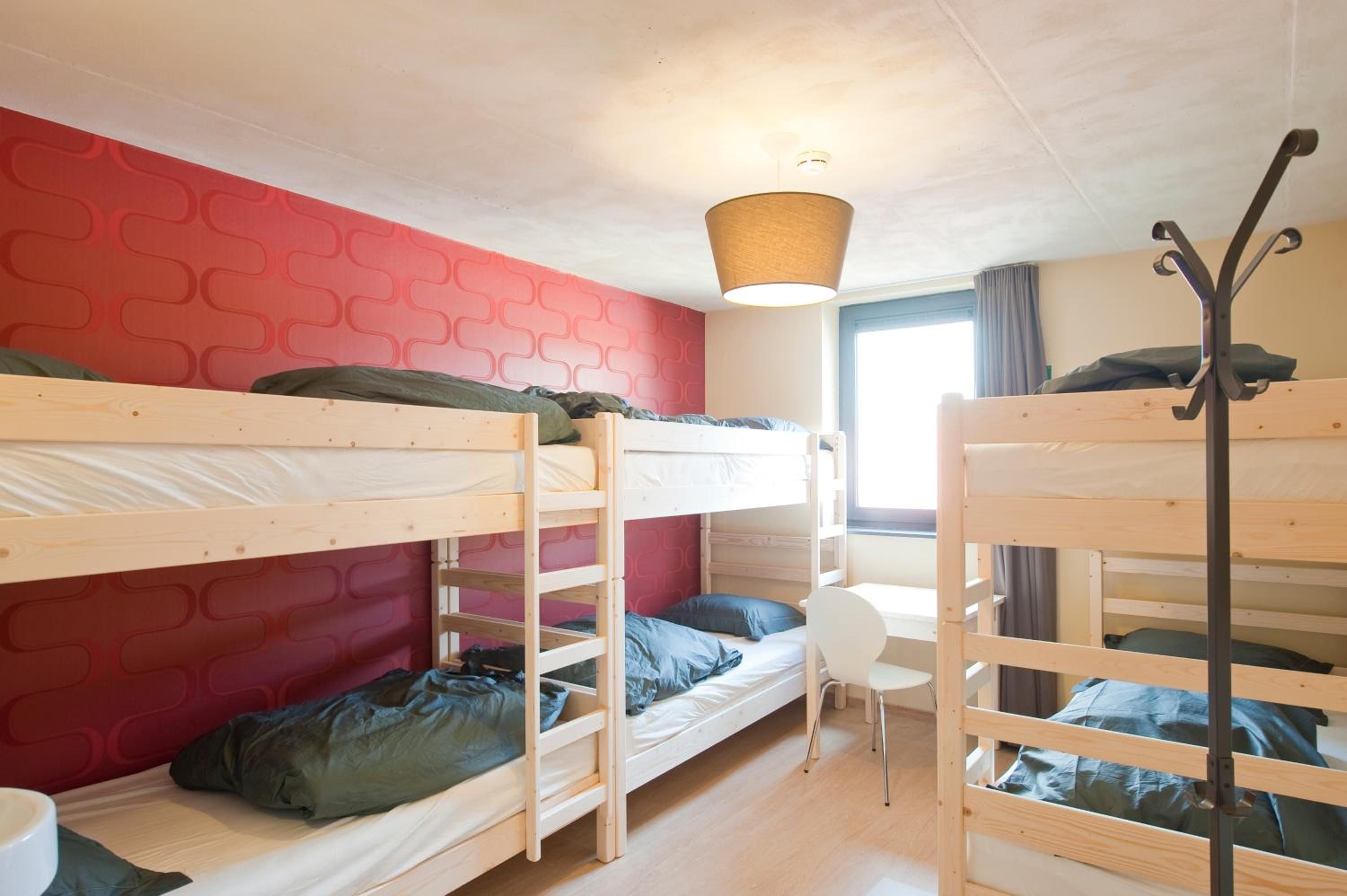 Een studentenkamer met stapelbedden, een klein bureau en een raam met gordijnen.