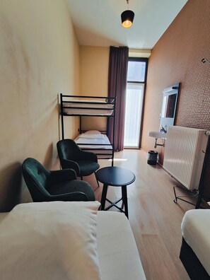 A compact hotel room with bunk beds, a small table, two chairs, a radiator, and a window with curtains. - Leuven City Hostel (Leuven)