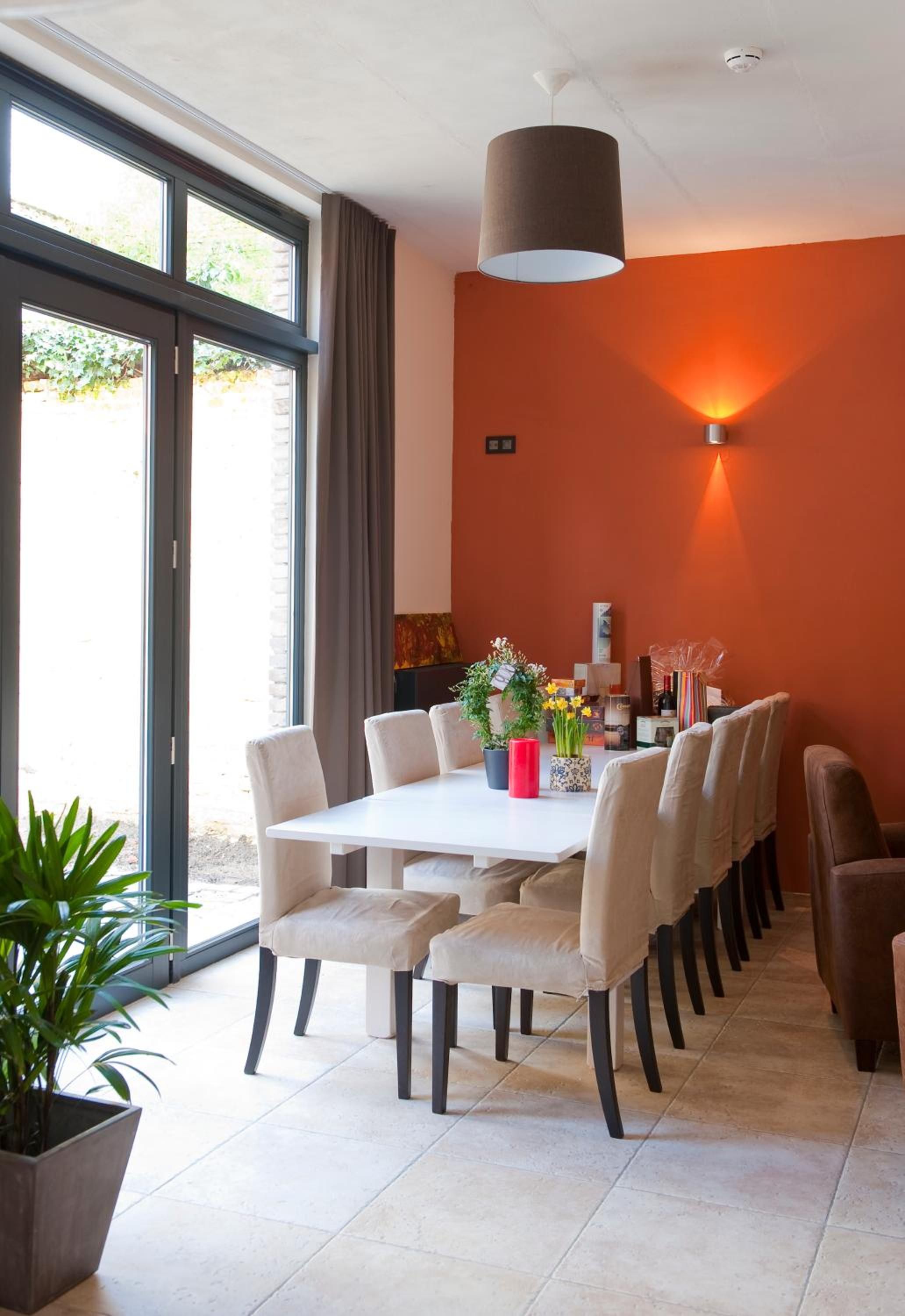 Un espace de salle à manger moderne avec une table et des chaises blanches, un grand luminaire suspendu et une vue à travers les portes vitrées.