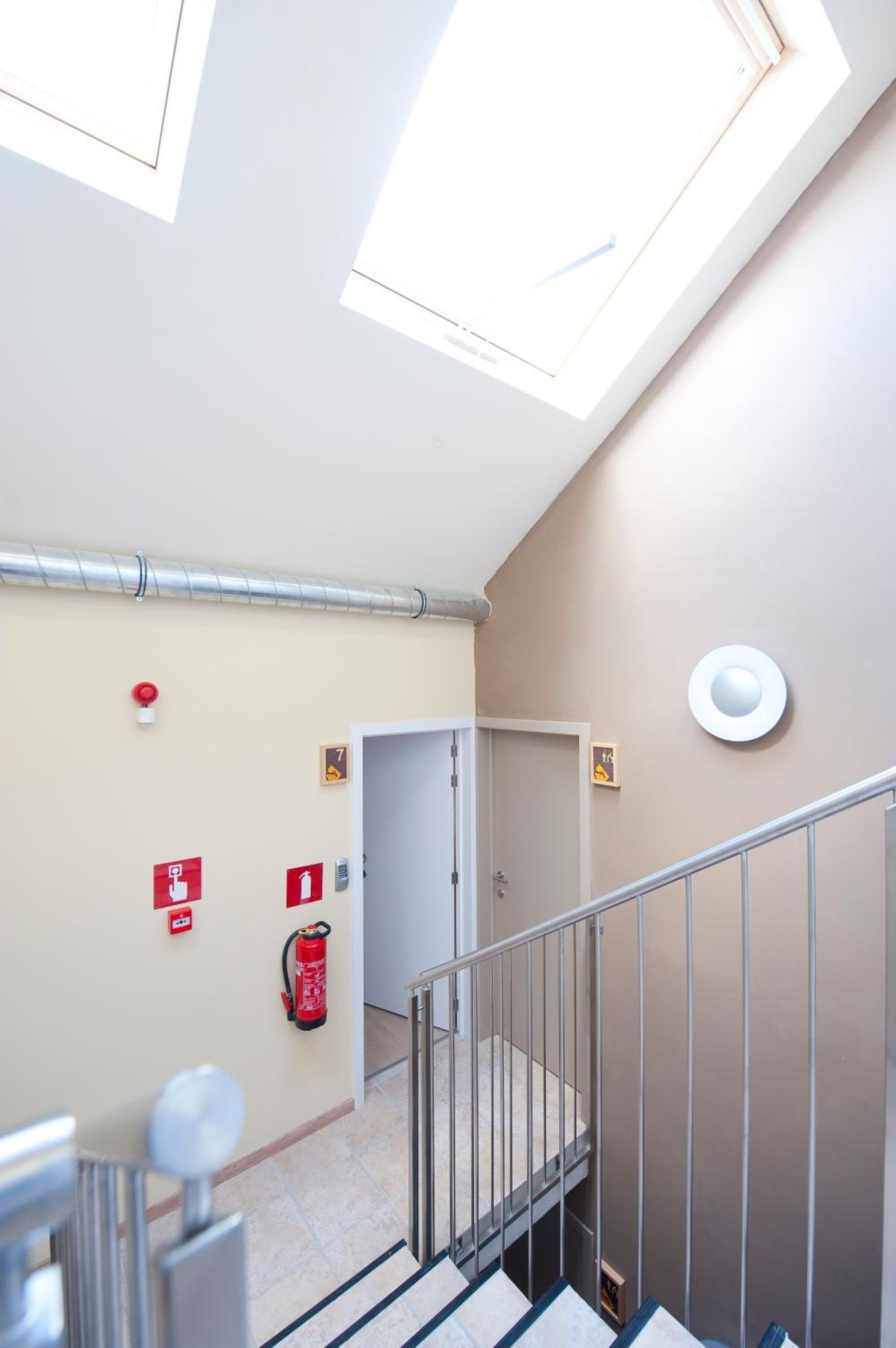 A stairwell with a fire extinguisher, emergency exit sign, and a door leading to another room.
