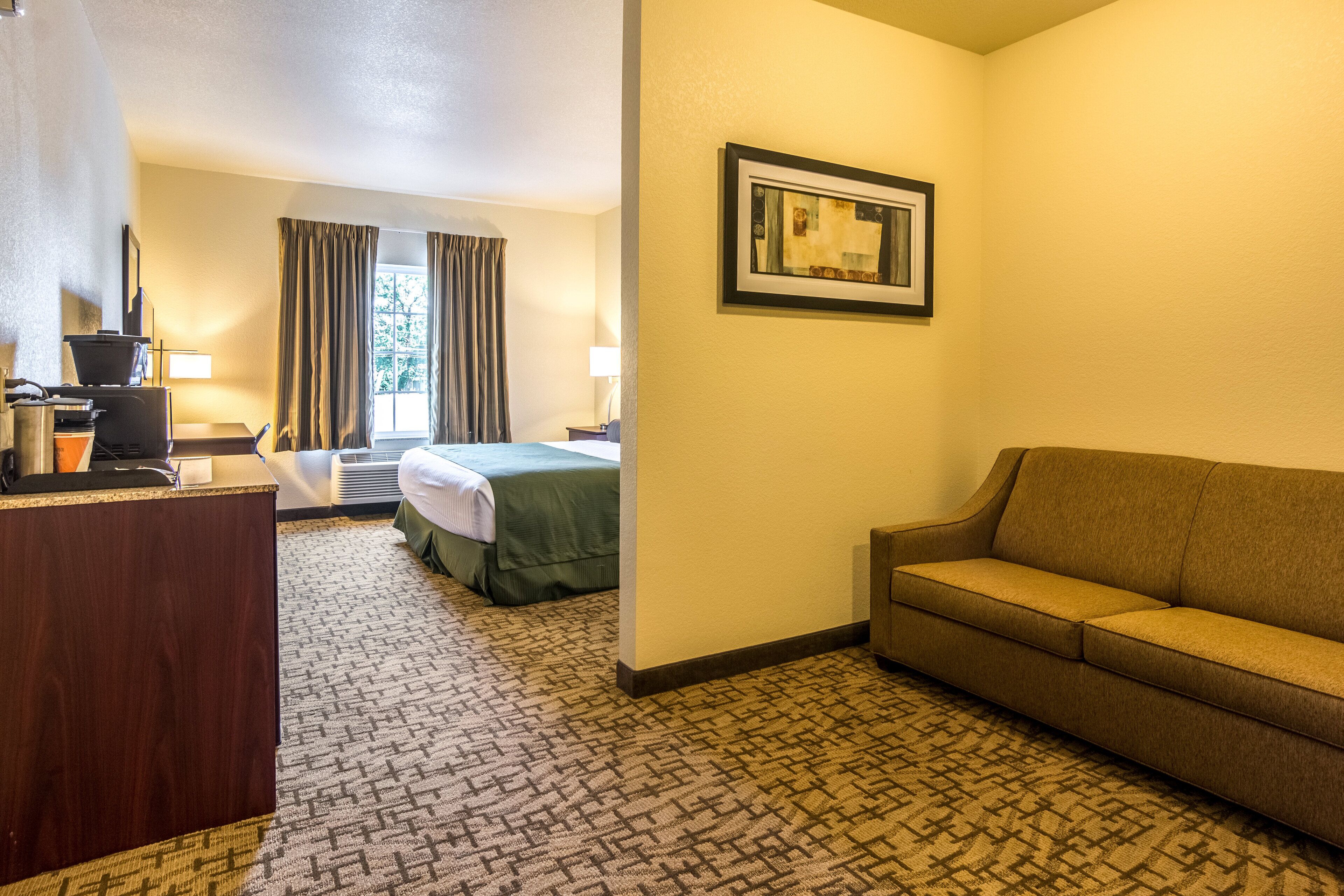 A hotel room with a desk, a bed, a sofa, and a framed picture on the wall.