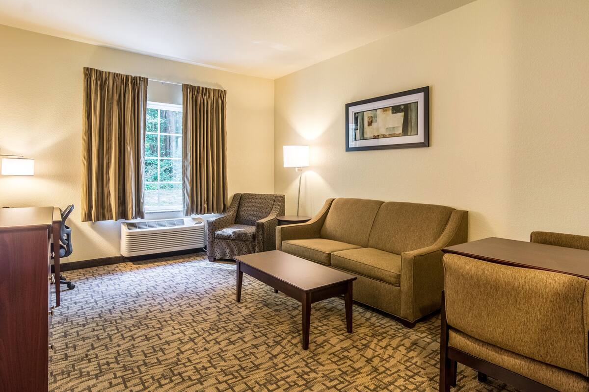 Une chambre d’hôtel équipée d’un canapé, d’un fauteuil, d’une table basse et d’un bureau avec une lampe.