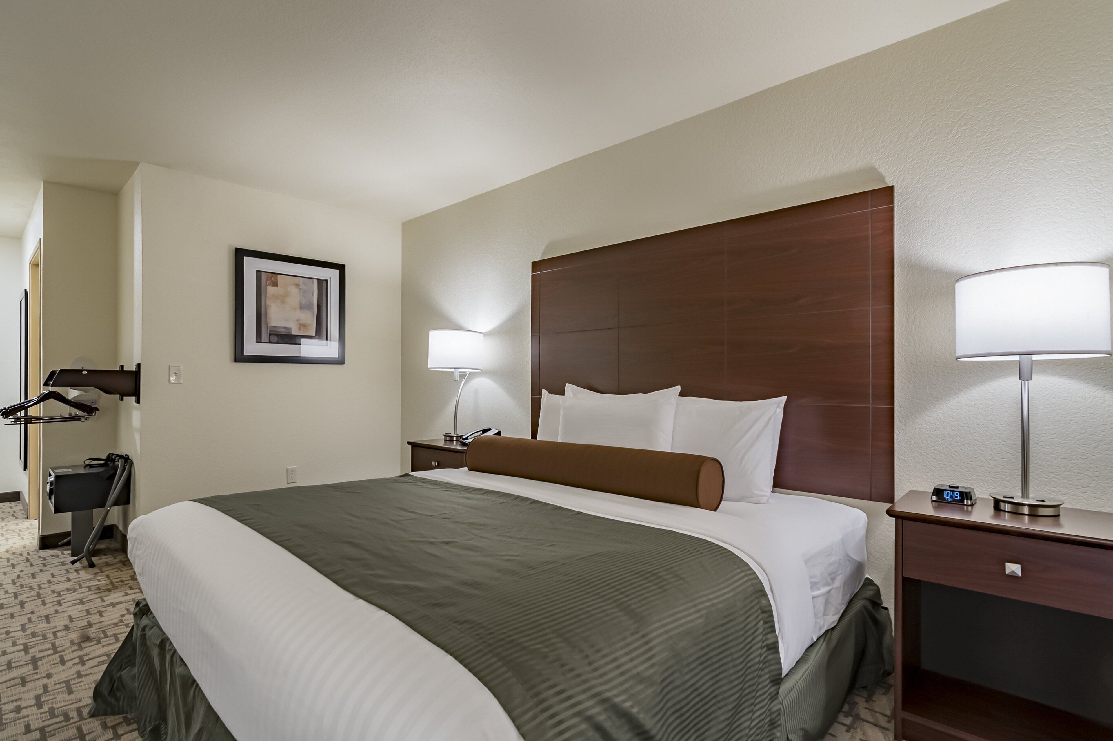 A hotel room with a large bed, a nightstand with a lamp, a wardrobe, and a framed picture on the wall.