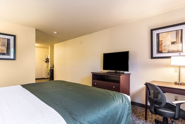 A hotel room with a bed, a desk with a chair, a television, and artwork on the walls.