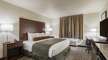 A hotel room with a large bed, two bedside tables with lamps, a desk with a chair, a television, and a window with curtains.