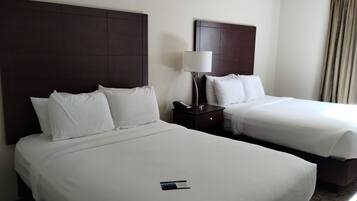 A hotel room with two beds, each with white linens and pillows. There is a nightstand with a lamp and a phone between the beds.