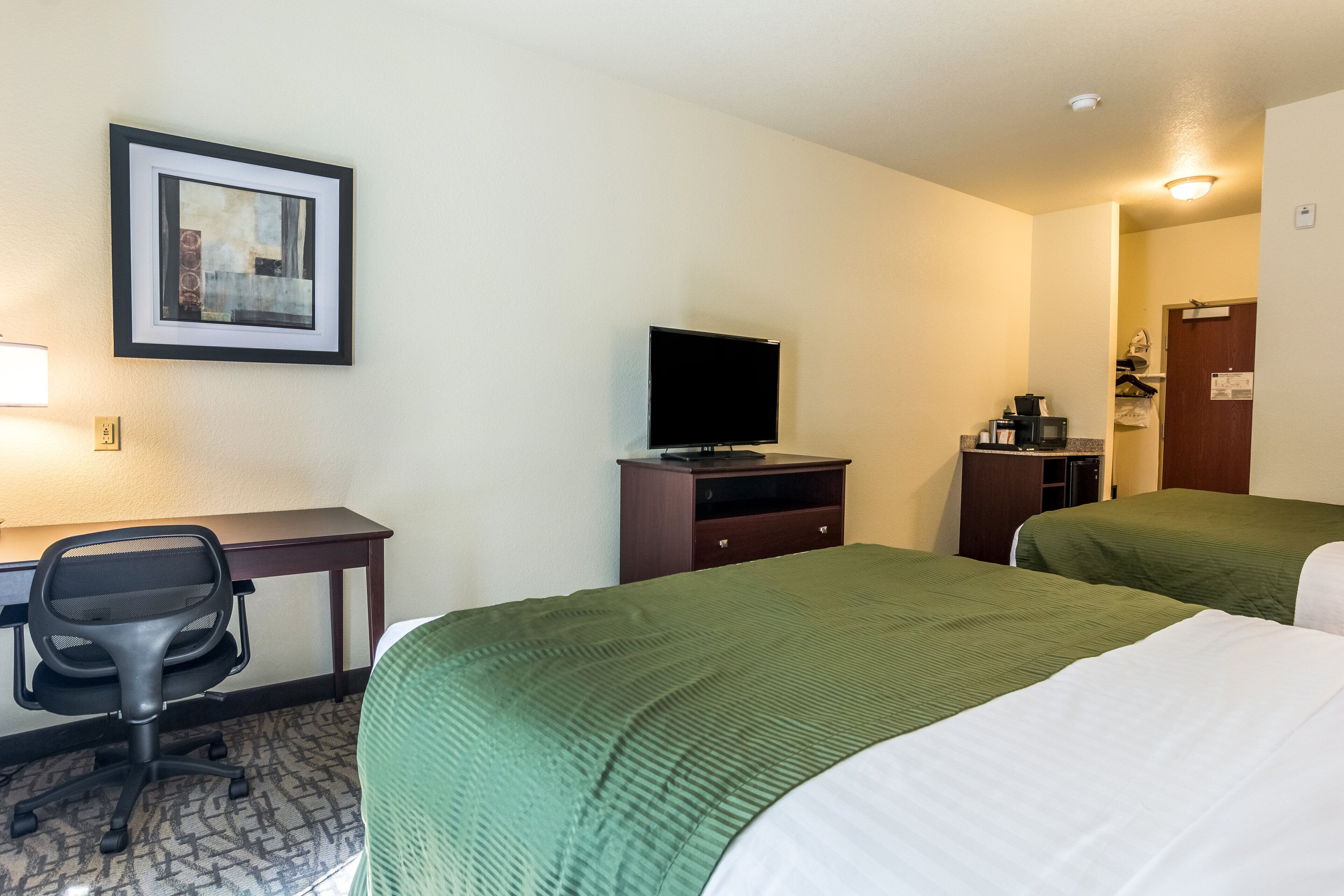 A hotel room with two beds, a desk with a chair, a television, and a framed picture on the wall.