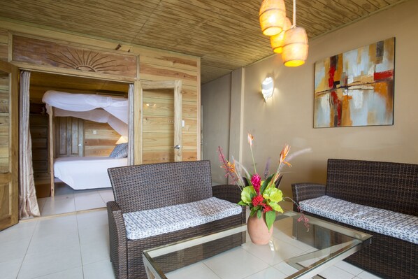 A room with a bed, two sofas, a glass coffee table, and a wall-mounted abstract painting.