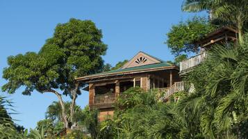 A wooden house with a balcony, surrounded by lush greenery and trees.