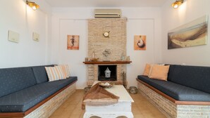 A living room with a brick fireplace, two sofas, a coffee table, and wall-mounted artwork. - Ammoudi Harmony Villa (Zakynthos)