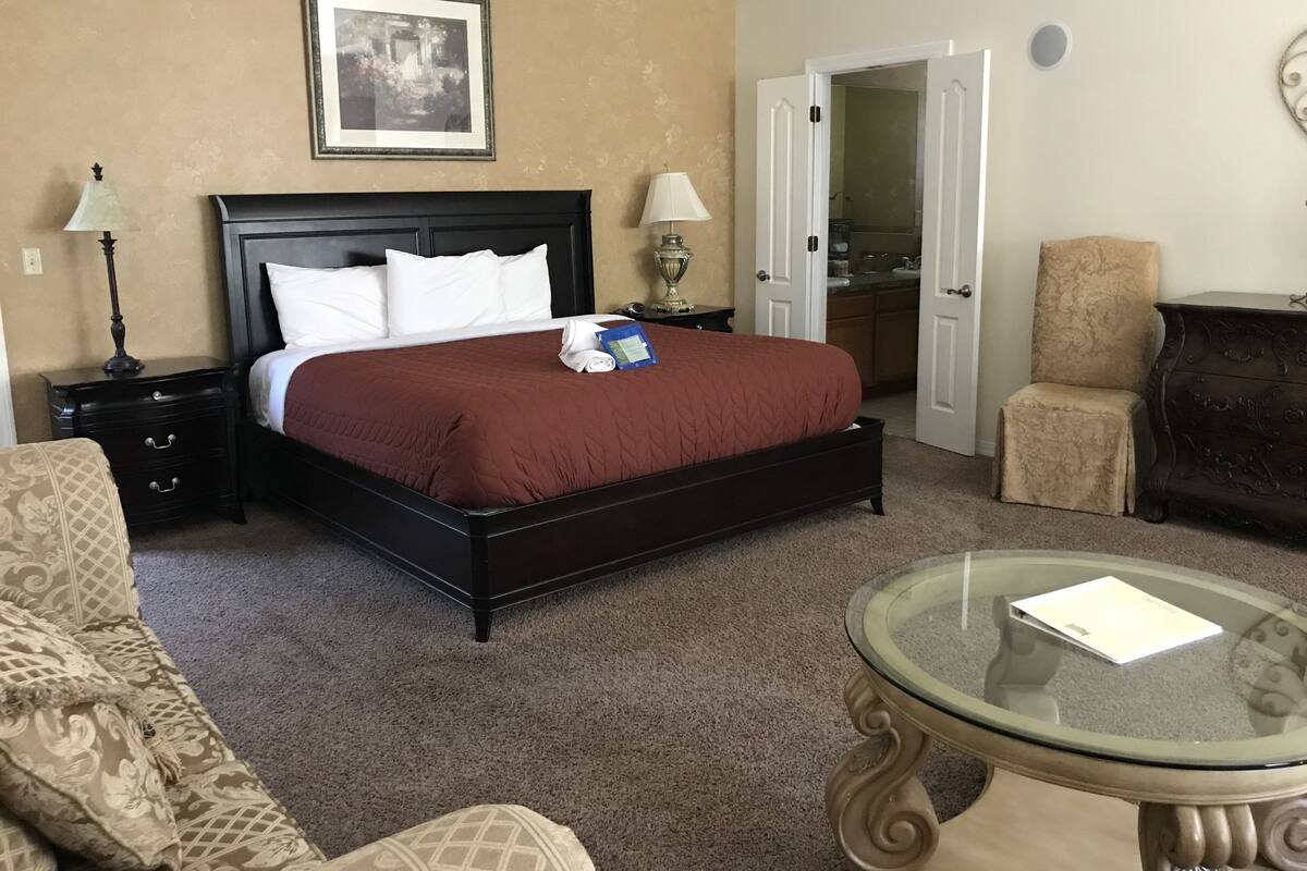A hotel room with a large bed, a glass coffee table, a chair, and a desk with a lamp.