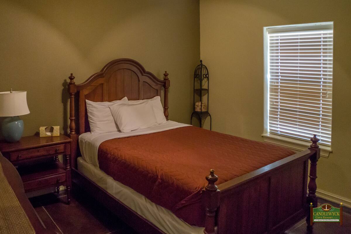 A single bed with a wooden headboard, a nightstand with a lamp, and a window with blinds.
