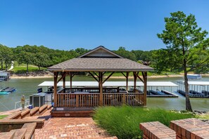Ein Pavillon mit Pflasterterrasse, mit Blick auf einen See mit Stegen und Booten.