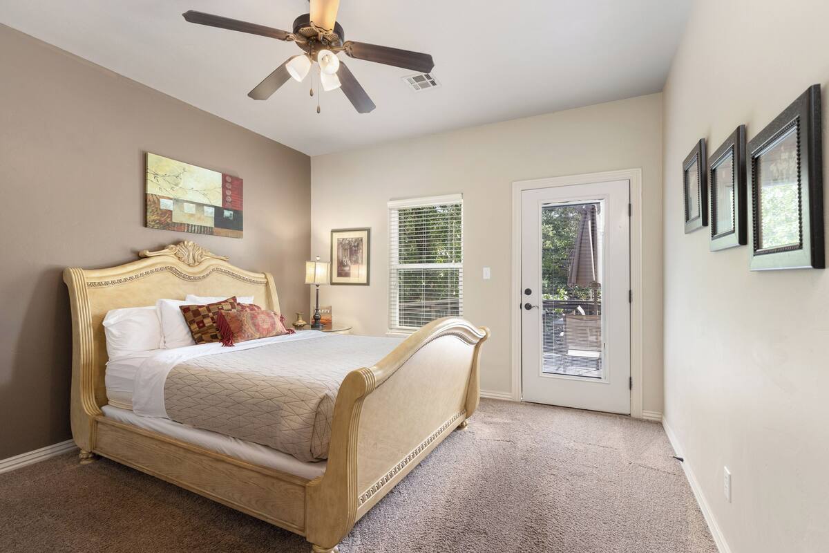 A bedroom with a bed, ceiling fan, artwork, and a door leading outside.