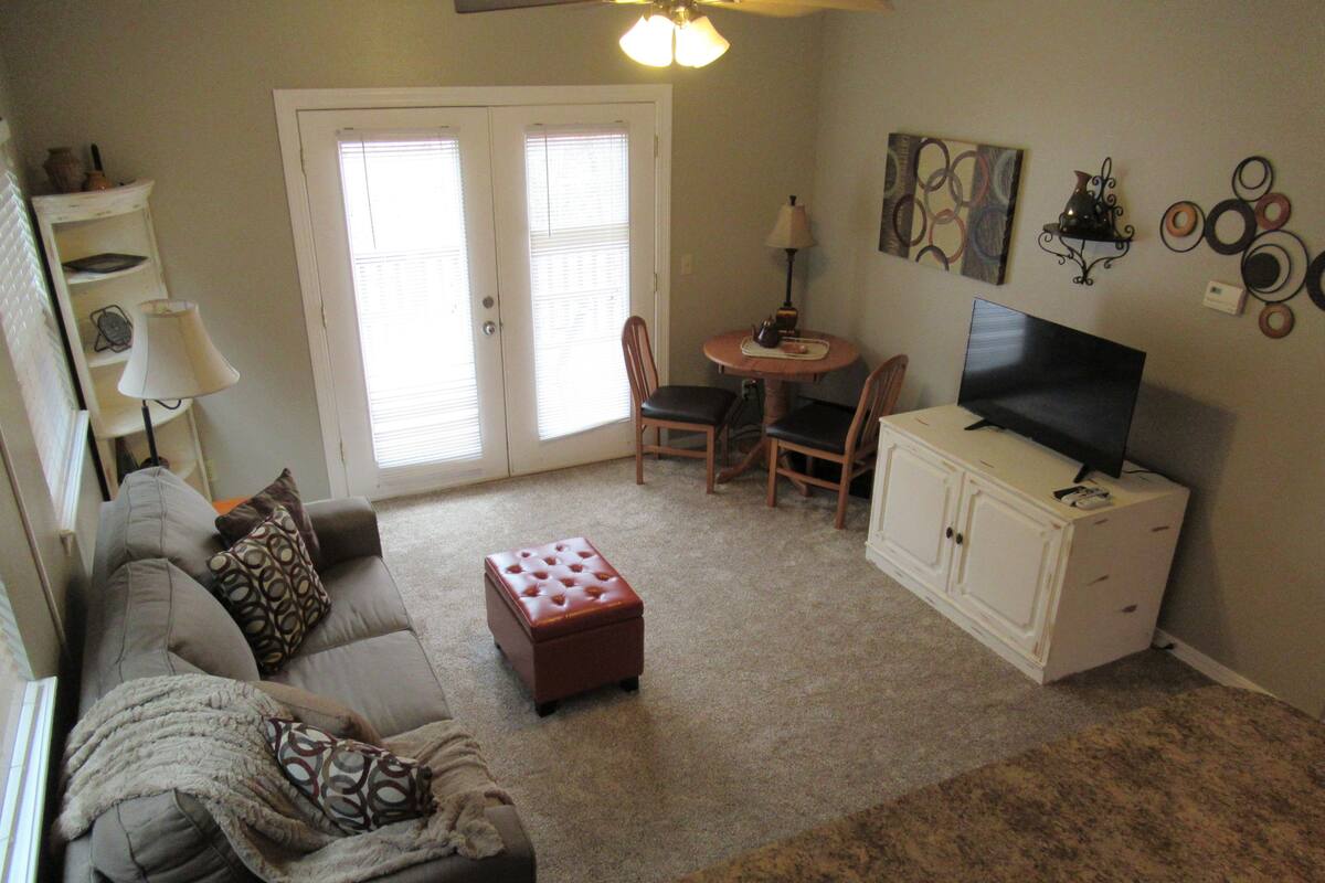 A living room with a sofa, ottoman, television, and a small table with chairs.