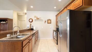 A kitchen with a stainless steel refrigerator, wooden cabinets, a double sink, and a tiled floor.