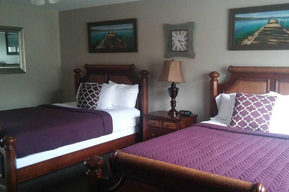 Two double beds with wooden headboards, a nightstand with a lamp, and a wall clock.