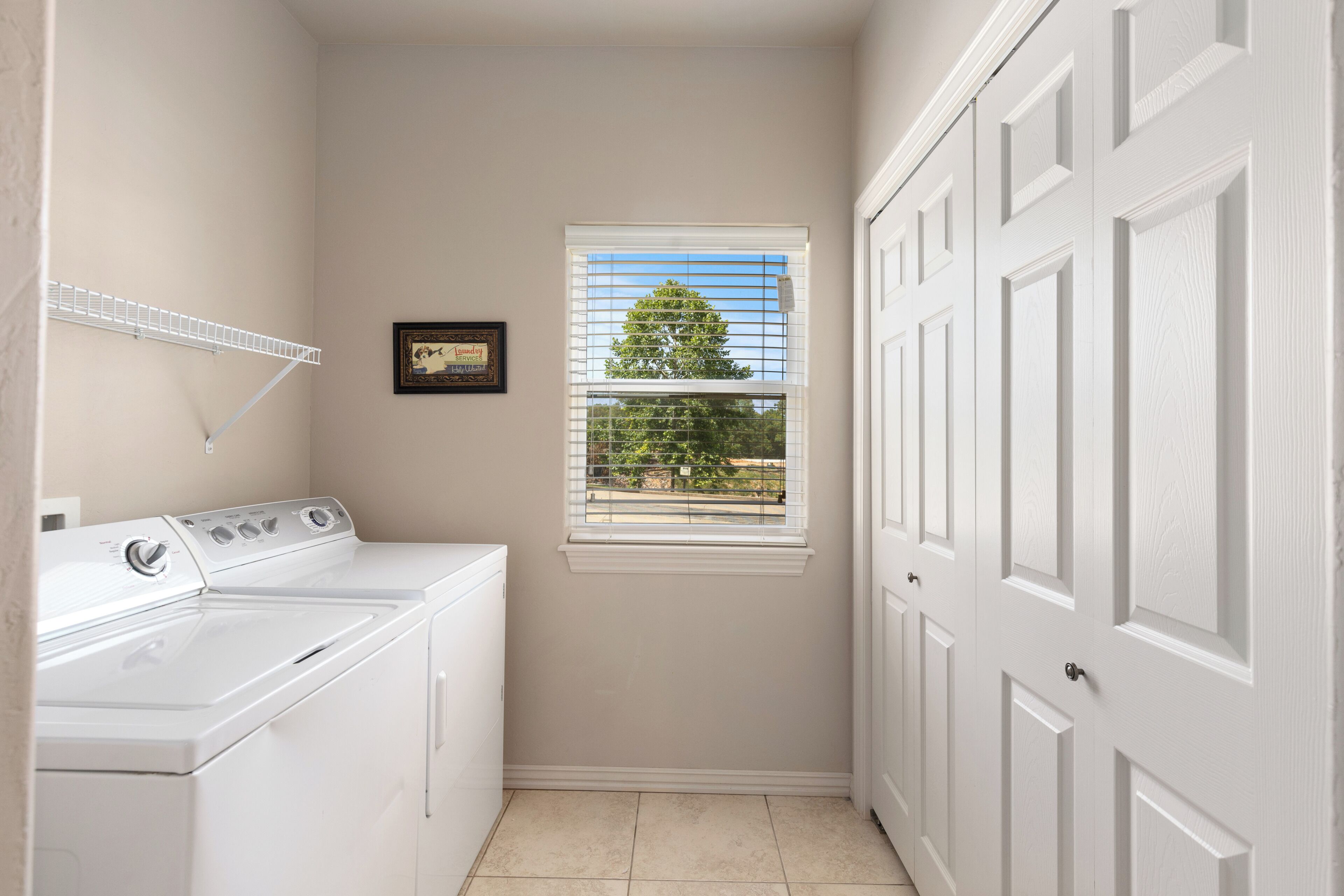 A laundry room with a washer and dryer, a window with blinds, and a door with a handle.
