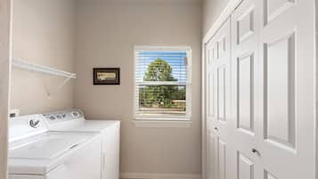A laundry room with a washer and dryer, a window with blinds, and a door with a handle.