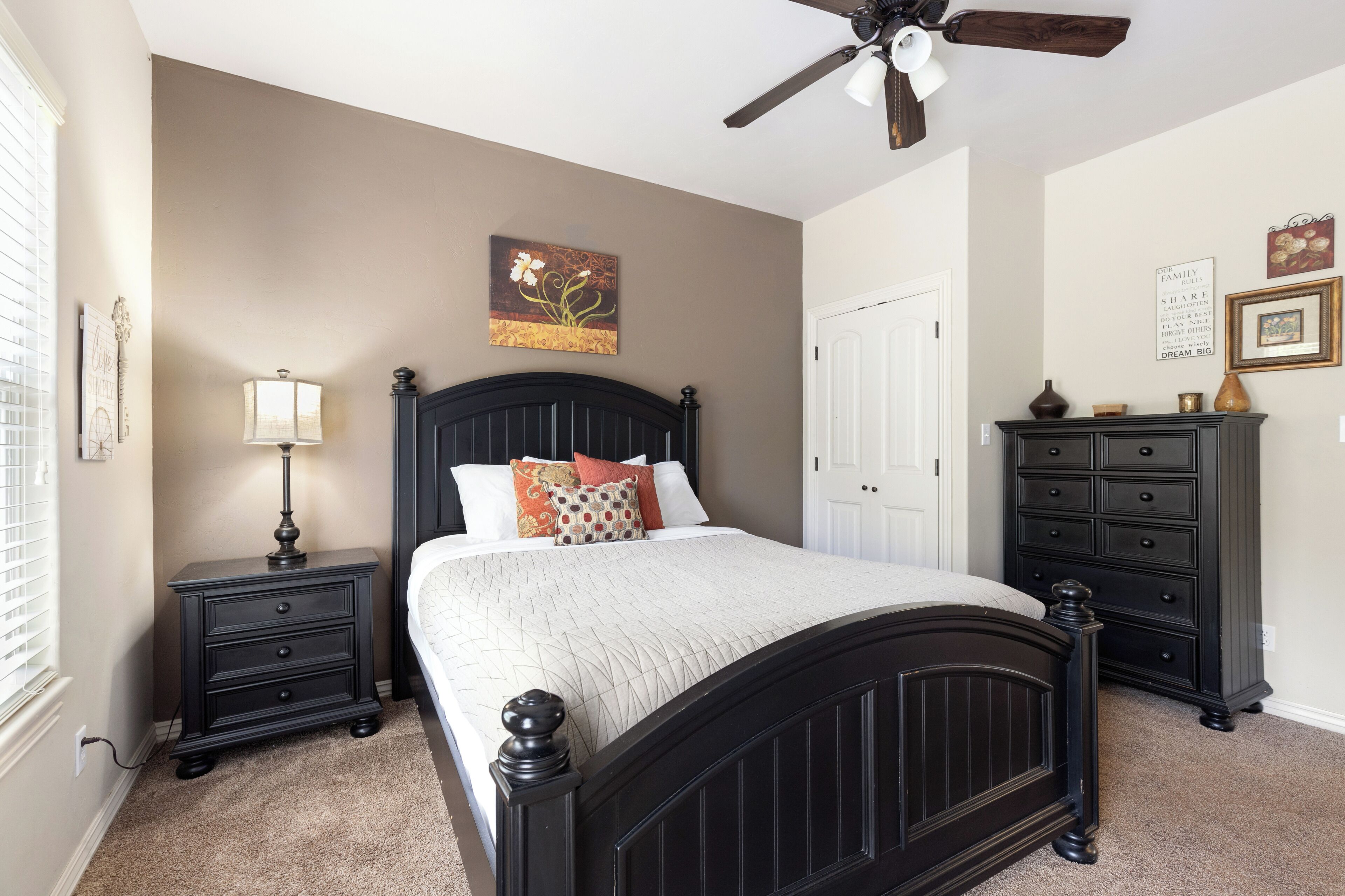 A bedroom with a bed, nightstands, a dresser, a ceiling fan, and artwork on the walls.