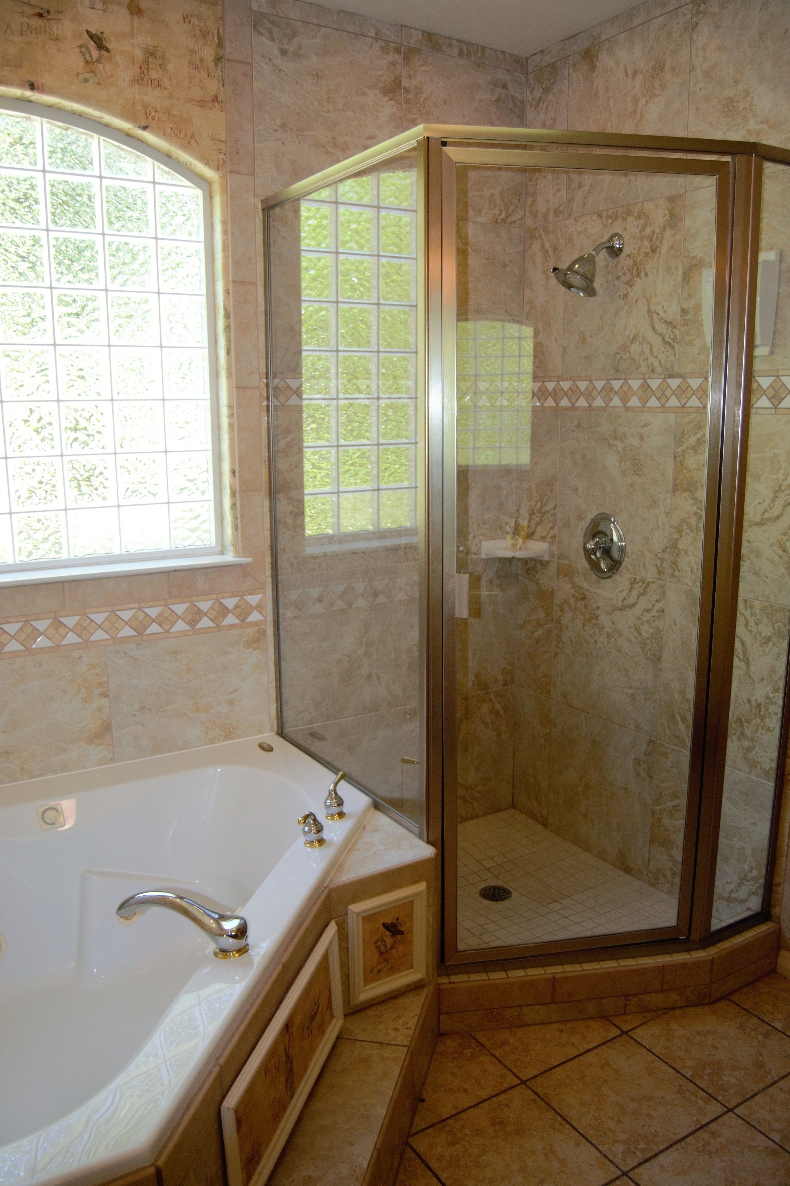 A bathroom with a glass-enclosed shower, a bathtub, and a window with a view of greenery.