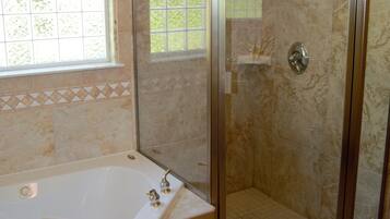 A bathroom with a glass-enclosed shower, a bathtub, and a window with a view of greenery.