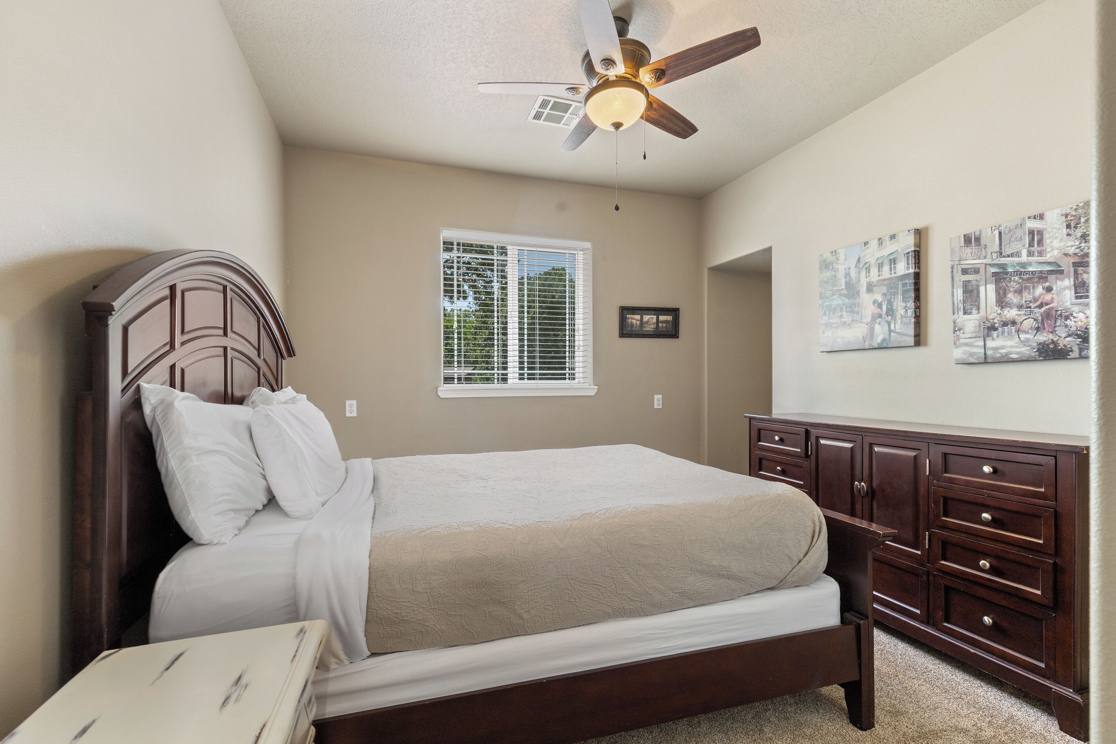 A bedroom with a bed, a dresser, a ceiling fan, and a window with blinds.