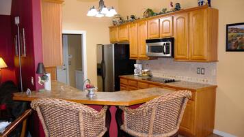 A kitchen with wooden cabinets, a stainless steel refrigerator, a microwave, and a granite countertop.