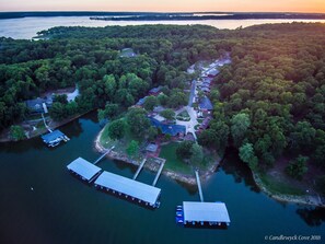 An aerial view of a lakeside property with docks, a marina, and residential buildings surrounded by dense forest. - Candlewyck Cove Resort (Grove)