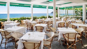 A restaurant with outdoor seating overlooking the ocean, featuring white tables and wicker chairs. - Hotel Beau Sejour (Alassio)