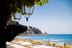 Una playa con hileras de sombrillas amarillas y carpas blancas, un cielo azul despejado y un paisaje montañoso al fondo.