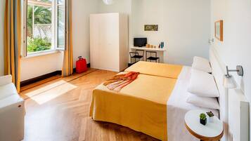 Une chambre d’hôtel avec un lit, un bureau, une chaise, une télévision et une petite table agrémentée de plantes.