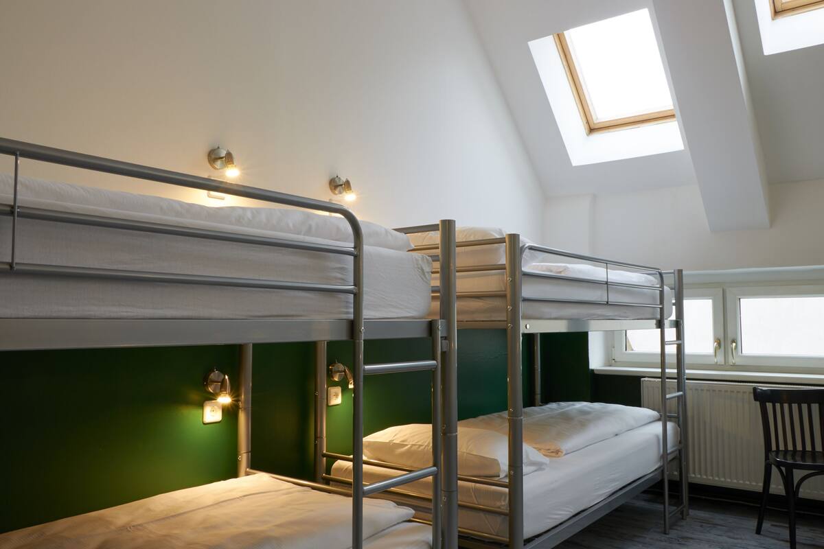 A dormitory room with bunk beds, a desk, and a chair.