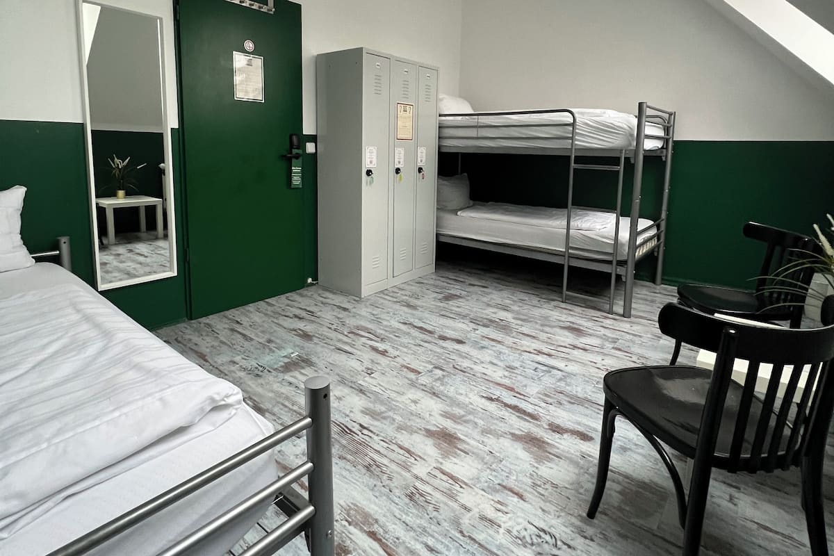 A dormitory room with bunk beds, a desk, a chair, a mirror, and a wardrobe.