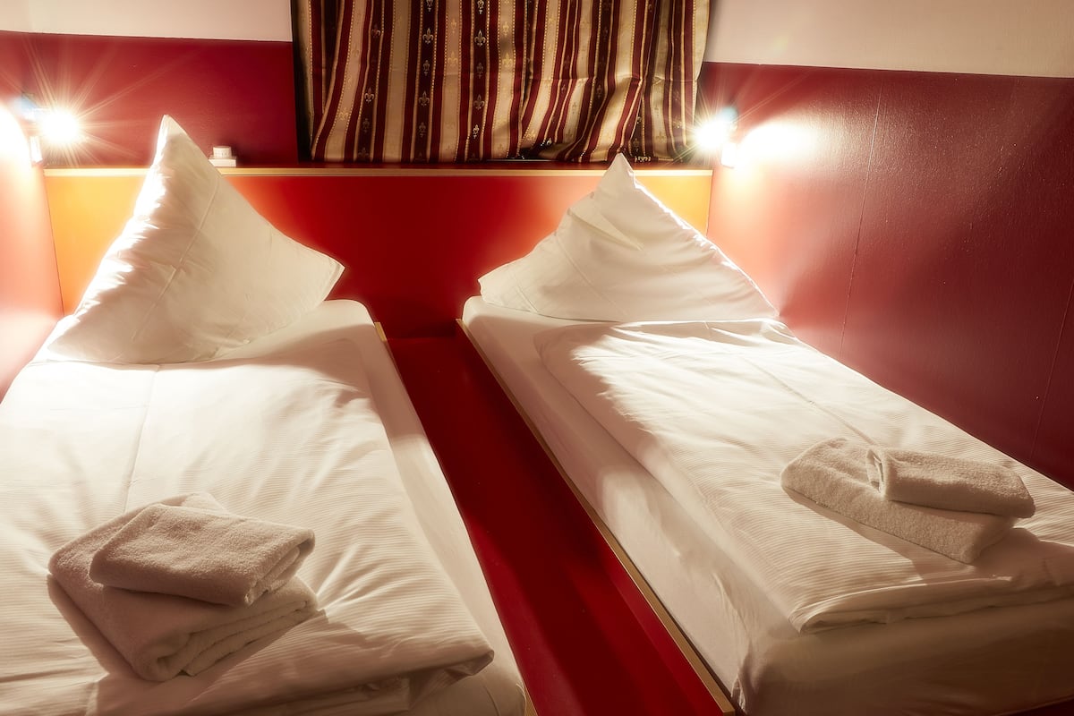 Two single beds with white linens and towels, a red wall, and a striped curtain.