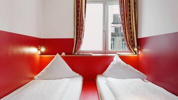 Una habitación con dos camas individuales, una ventana con cortinas y una pared de acento roja.