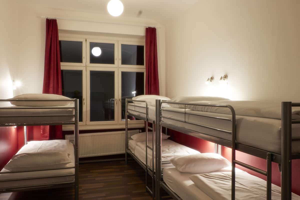 A dormitory room with bunk beds, a window with curtains, and a radiator.