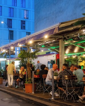 An outdoor seating area with tables and chairs, surrounded by potted plants and a building in the background. - Ballhaus Berlin Hostel (Berlin)