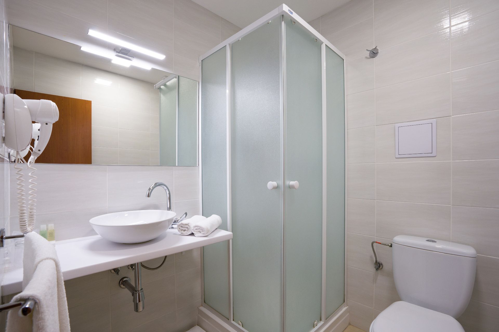 Un baño con lavamanos blanco, un espejo, cabina de ducha de vidrio y un inodoro.
