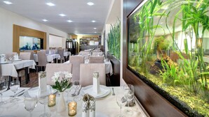 Un restaurant où les tables sont dressées pour le service, avec un grand aquarium sur un des murs et une vue sur l’intérieur du restaurant.