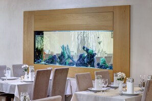 Un espace repas avec des tables dressées pour le service, agrémenté d’un grand aquarium placé derrière les tables.