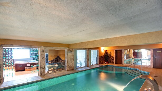 Une piscine intérieure avec un mur en pierre, un espace détente et une vue sur l’extérieur.